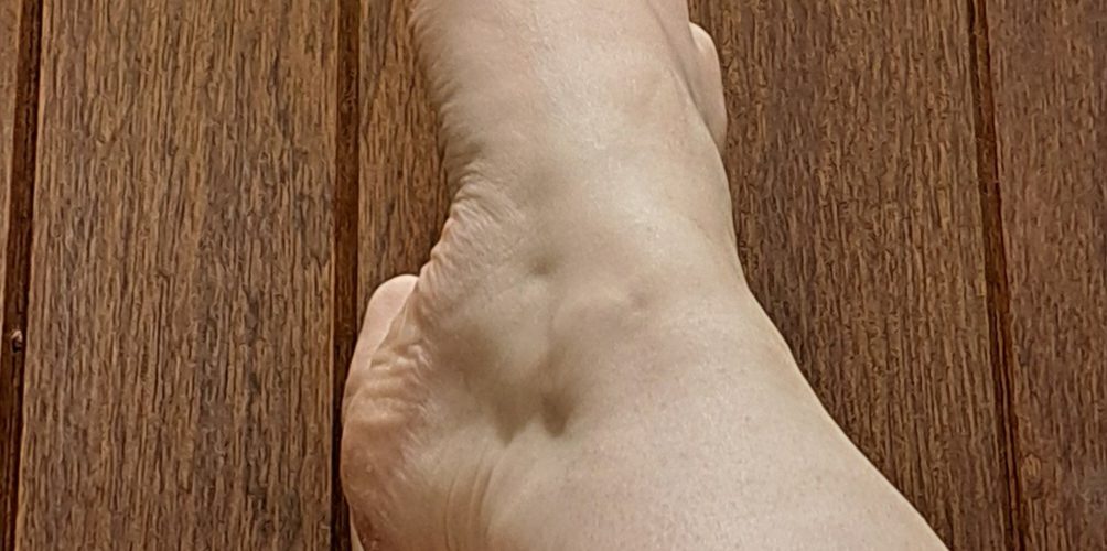 Unclothed feet & legs, crossed at the ankle, against a wooden surface.