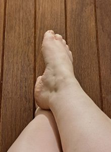 Unclothed feet & legs, crossed at the ankle, against a wooden surface.